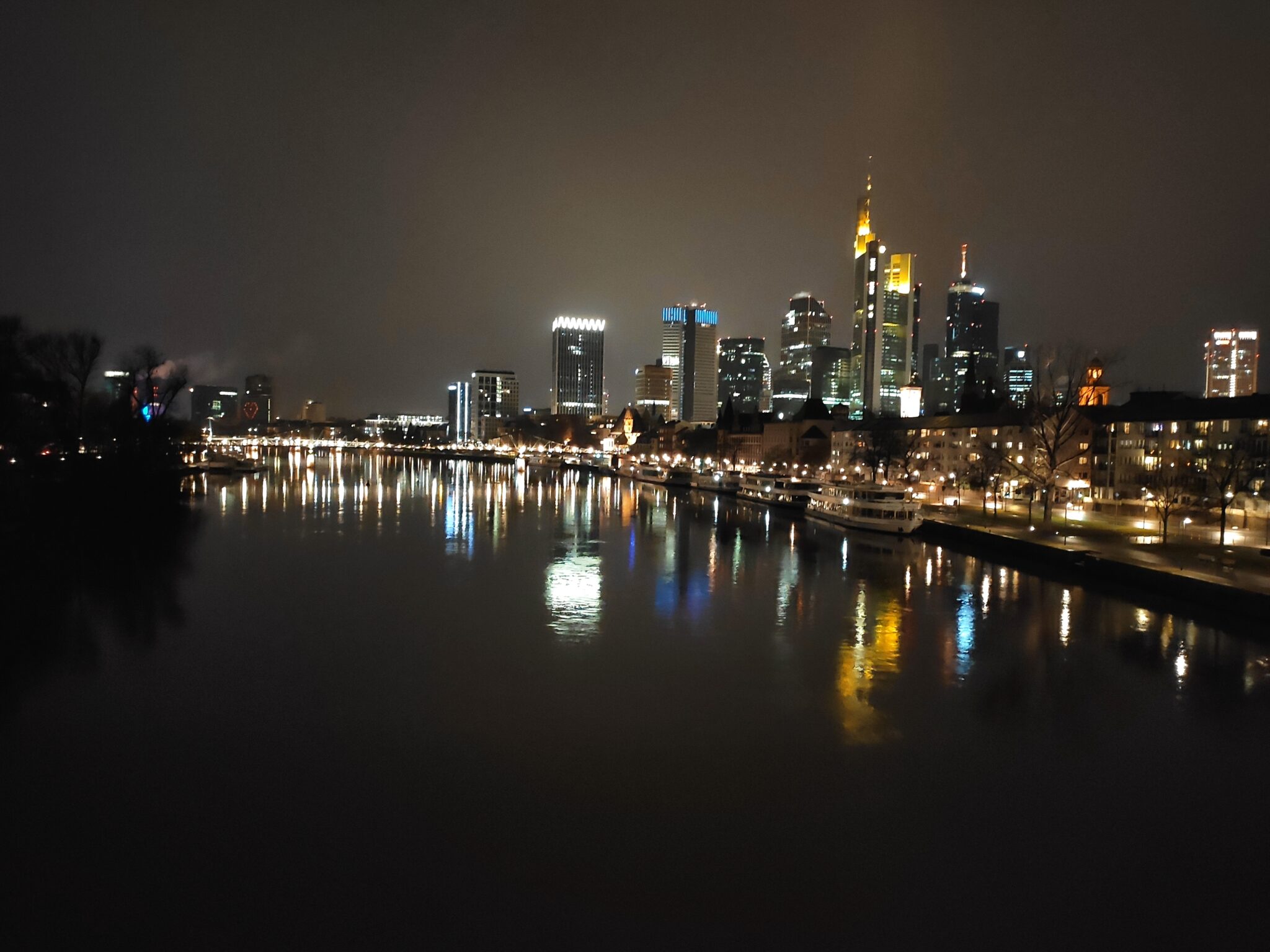 Die erleuchtete Frankfurter Skyline bei Nacht, die sich im Main spiegeln. 